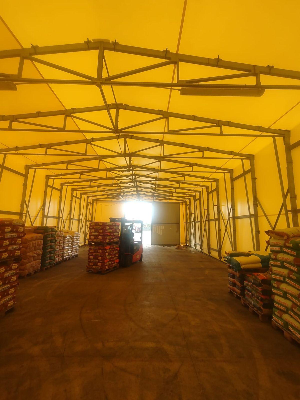 Interno di un magazzino in telo PVC con teli nuovi, pallet di sacchi e carrello elevatore