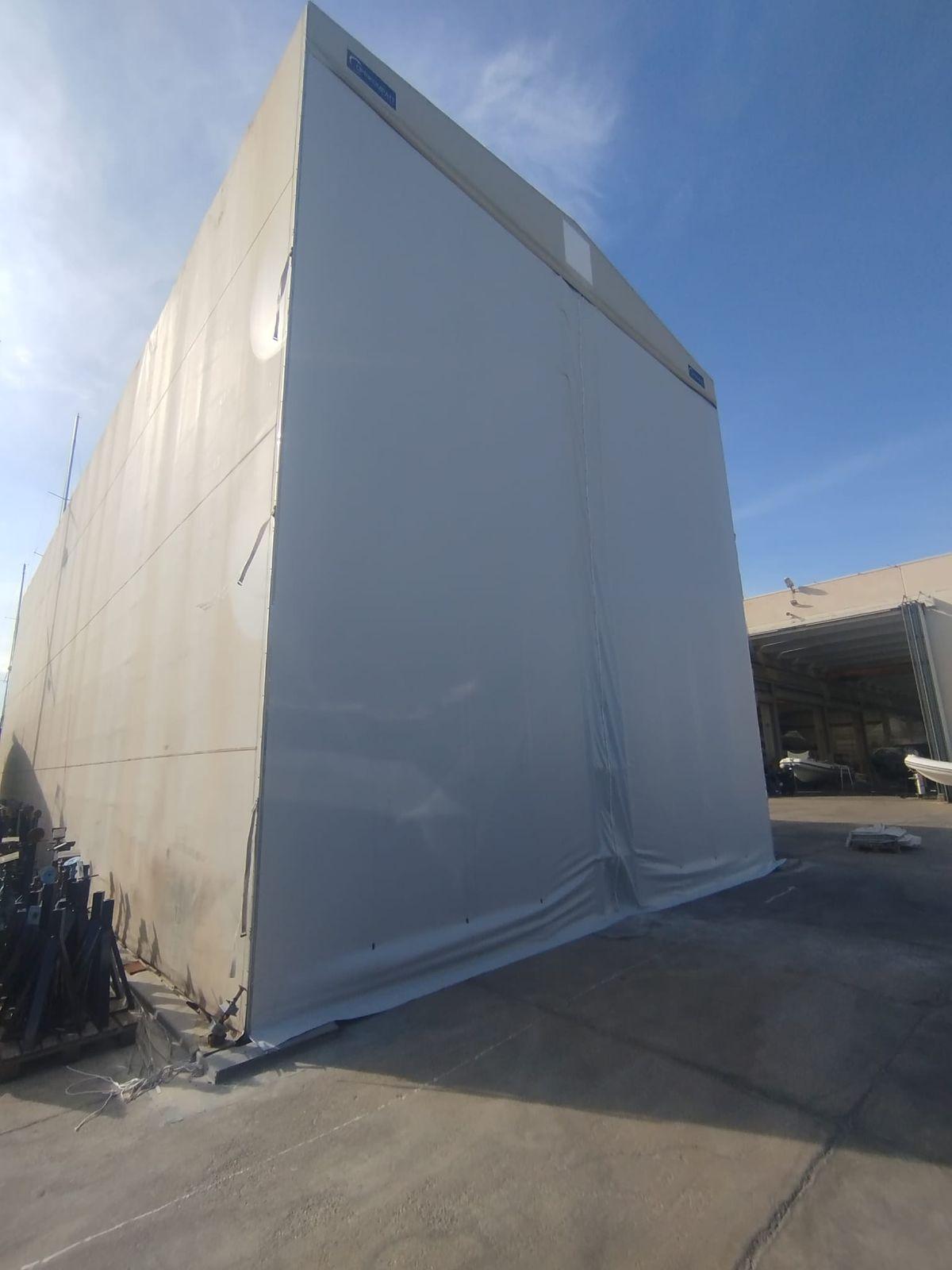 Capannone in telo di un cantiere navale con la testata in telo PVC nuova, bianca, accanto alla parete laterale originale ingrigita